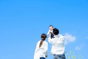 青空の下で赤ちゃんを抱き上げる夫婦